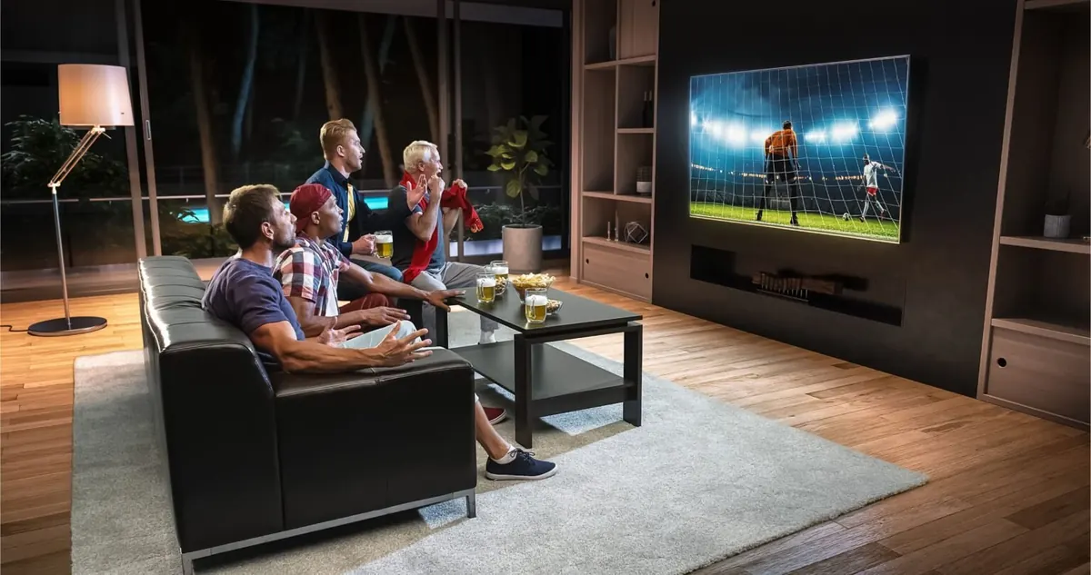 Friends cheering a live football match streamed on KROOZ TV on a large living-room TV